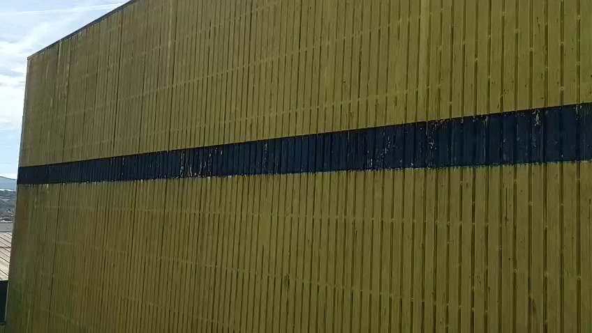 Fachada industrial amarilla con depósitos oscuros antes de la limpieza